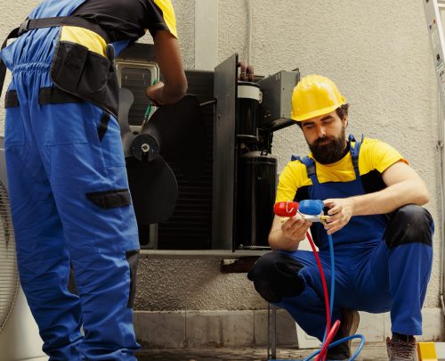 Seasoned mechanic getting rid of layer of dirt and dust from hvac system evaporator while coworker uses benchmarking tool to check for freon leaks and read pressure in air conditioner system
